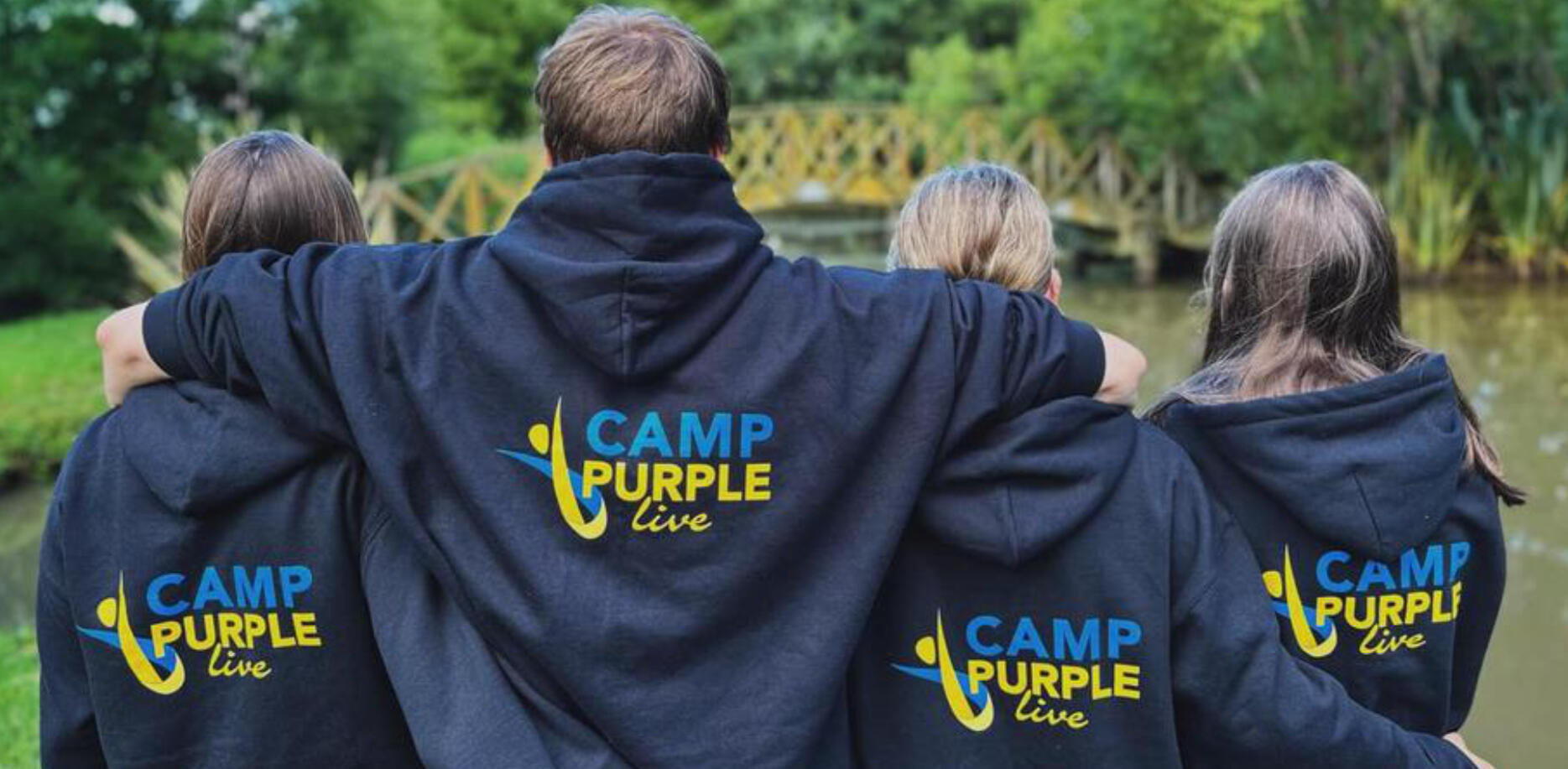 Four people wearing Camp Purple Live hoodies staring at a lake.